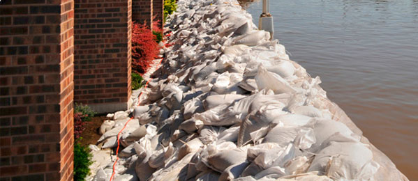 pile of sandbags between large brick building and body of water