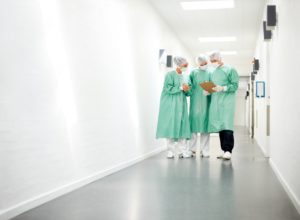 three physicians in scrubs in hospital hallway reading charts talking togther