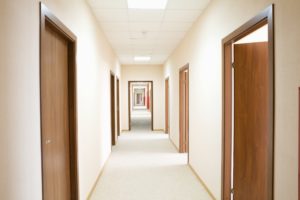 narrow hallway with brown doors some open and closed white paint on the wall